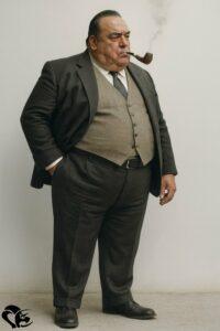 Laurent Chani, écrivain en costume trois-pièces, se tient debout avec assurance, une pipe fumante à la bouche | Laurent Chani, writer in a three-piece suit, stands confidently with a smoking pipe in his mouth